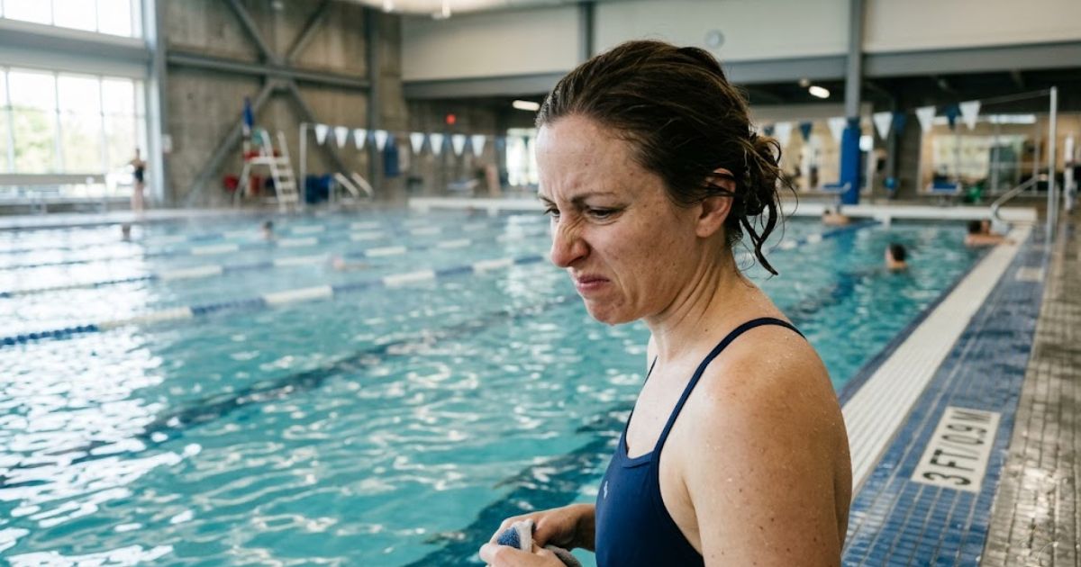 pool chlorine smell causes — person reacting to strong chemical odor at indoor swimming pool