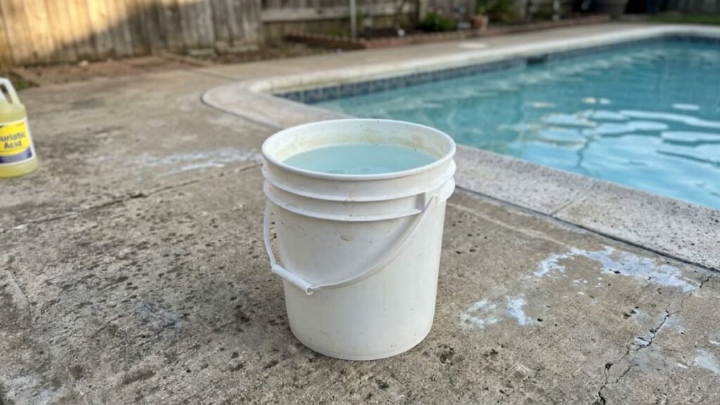 White plastic bucket three-quarters full of pool water on concrete deck for diluting muriatic acid before adding to pool