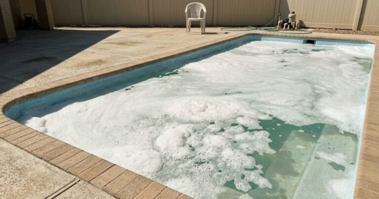 Thick white foam floating on pool water surface near steps of a residential backyard pool