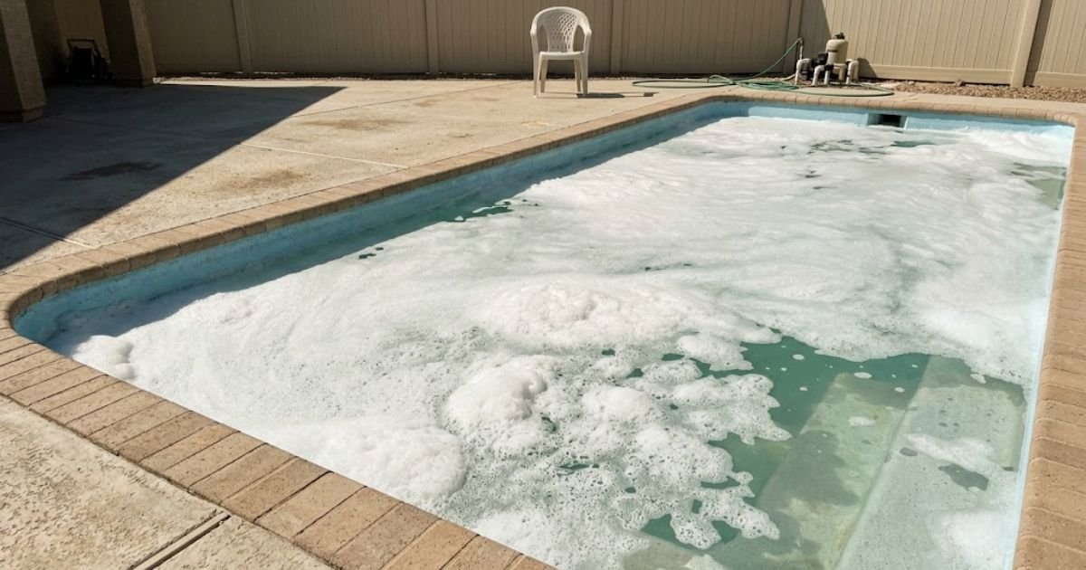 Thick white foam floating on pool water surface near steps of a residential backyard pool