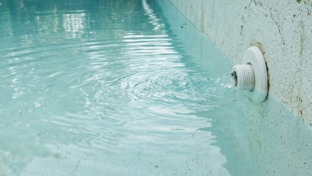 Pool return jet in deep end of backyard swimming pool showing correct location to pour diluted muriatic acid for pH correction