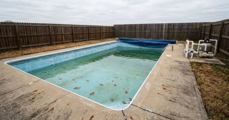 Inground pool in a suburban backyard being prepared for winter with leaves on the deck in October