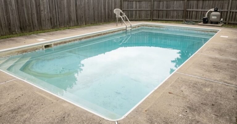 Residential inground pool with slightly hazy water and visible biofilm ring on waterline tile in a normal suburban backyard